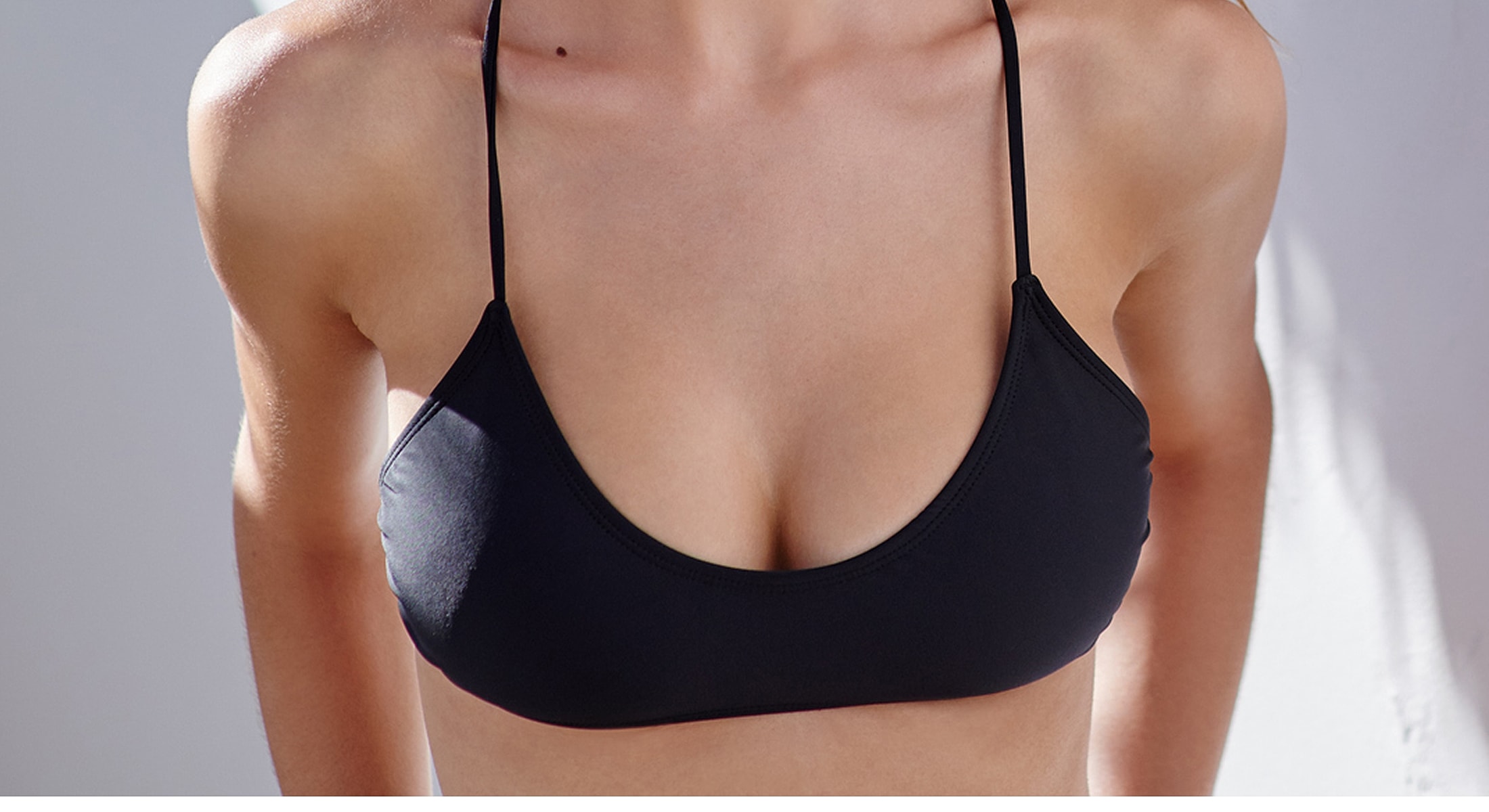 Model in black bikini top against light backdrop.