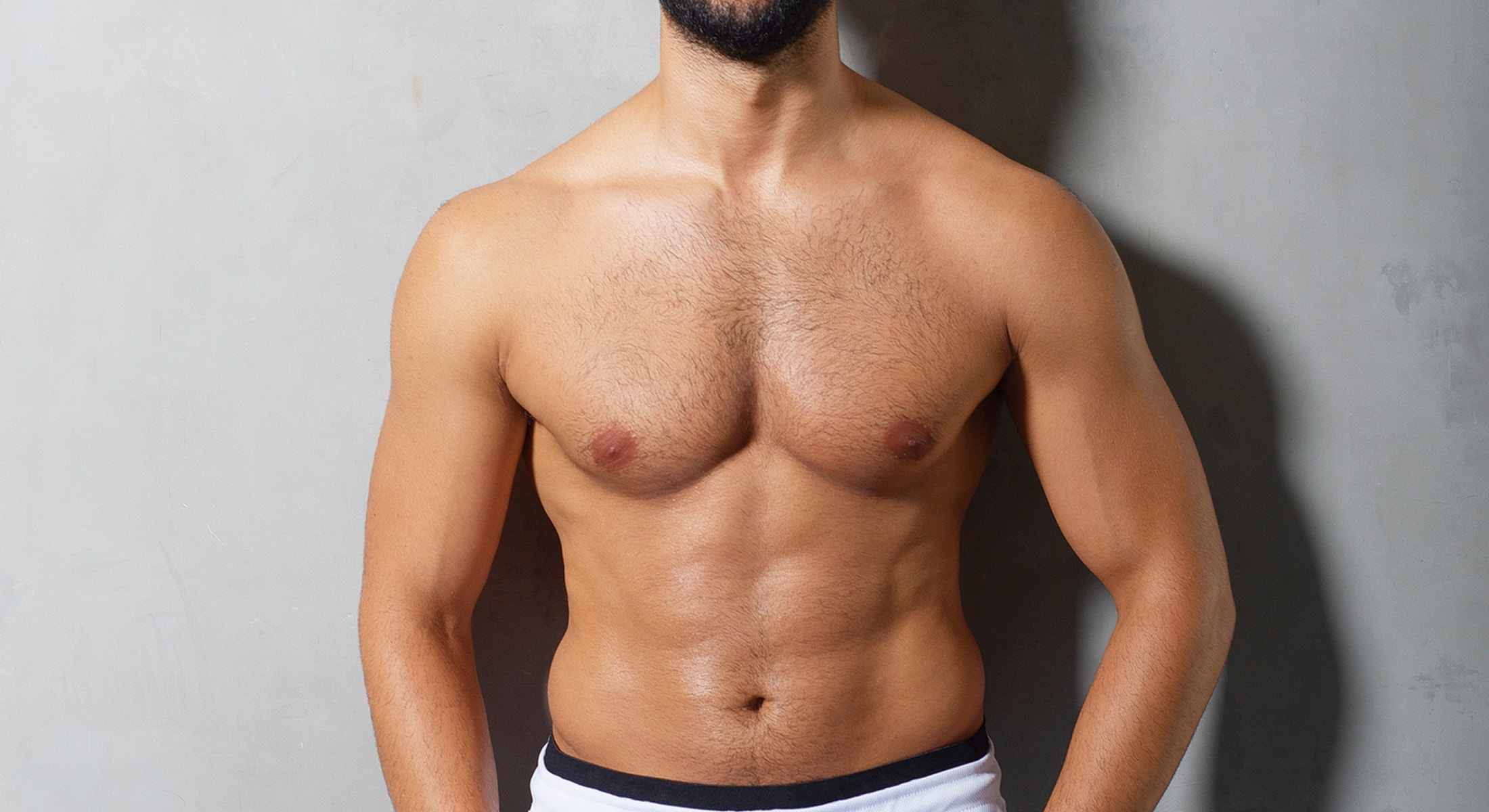 Male model showing toned physique against gray background.